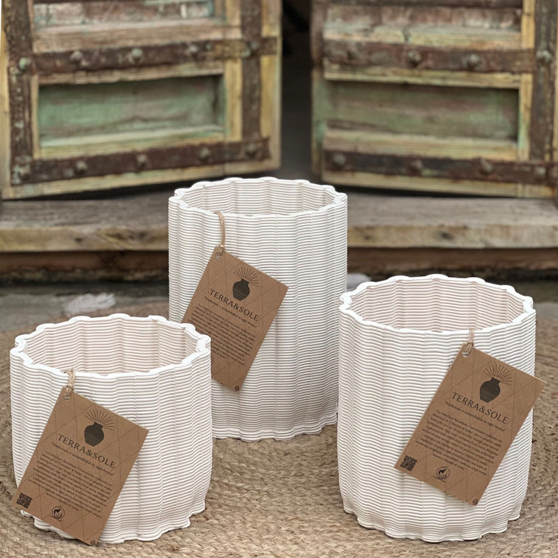 Set di tre vasi Giulia in argilla bianca naturale con etichette Terra&Sole, disposti su tappeto in fibra davanti a portone rustico.