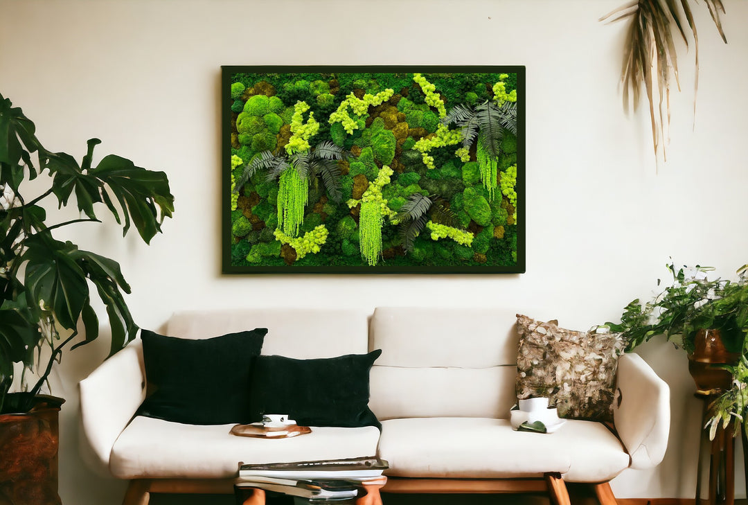 Quadro di verde stabilizzato di forma rettangolare, su parete bianca con sofà moderno sotto cuscini verdi e piante verdi e rigogliose . 