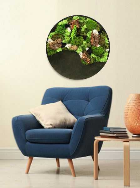 Un quadro circolare di piante verdi stabilizzate appeso sopra una poltrona blu in un interno moderno.
