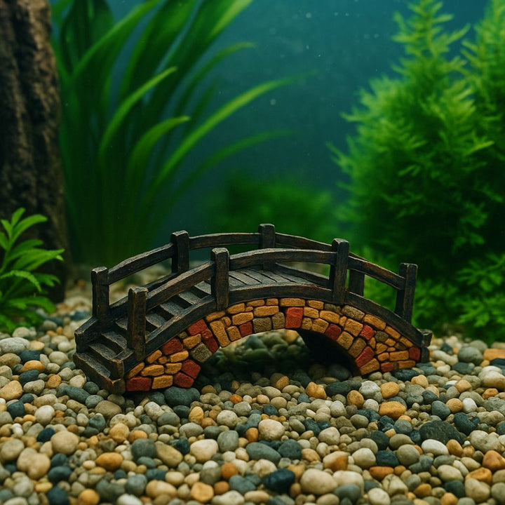 Ponte decorativo in resina effetto pietra, immerso in acquario con ghiaia e piante acquatiche sullo sfondo.