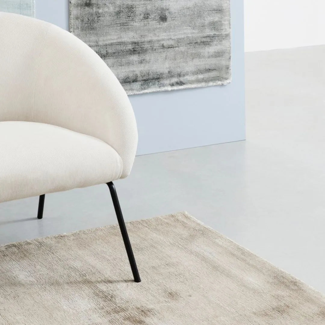 Tappeto Rashmi beige posizionato sotto poltrona bianca

