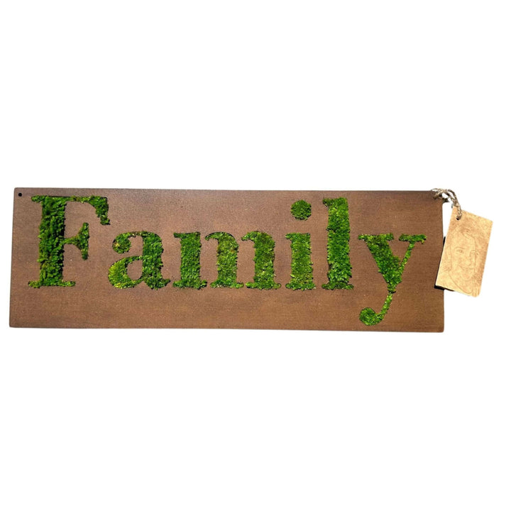 Targa rettangolare in legno con la parola “Family” intagliata e riempita di muschio stabilizzato verde. La targa ha un cordino con etichetta artigianale appesa sul lato destro.