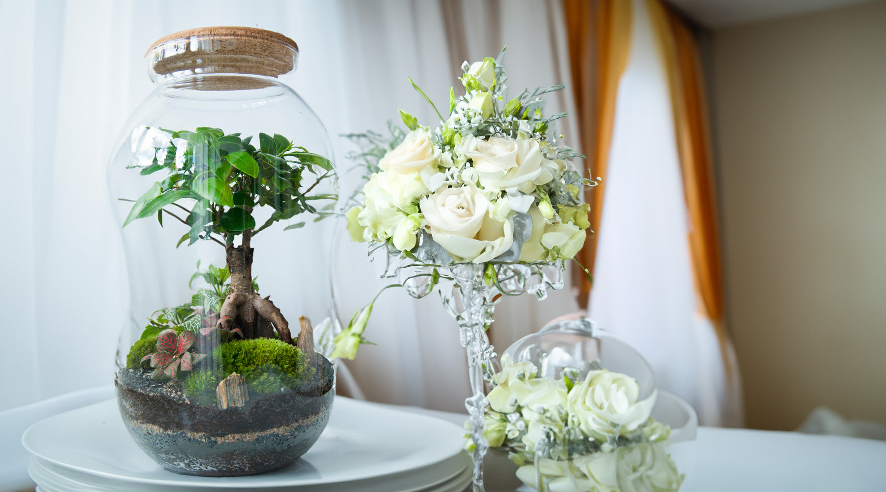 L'immagine mostra Un terrarium elegante affianco a dei bouquet wedding di rose bianche 