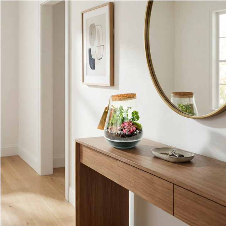 Terrarium in vetro con piante tropicali posizionato su mobile da ingresso con specchio, decorazione naturale elegante per casa