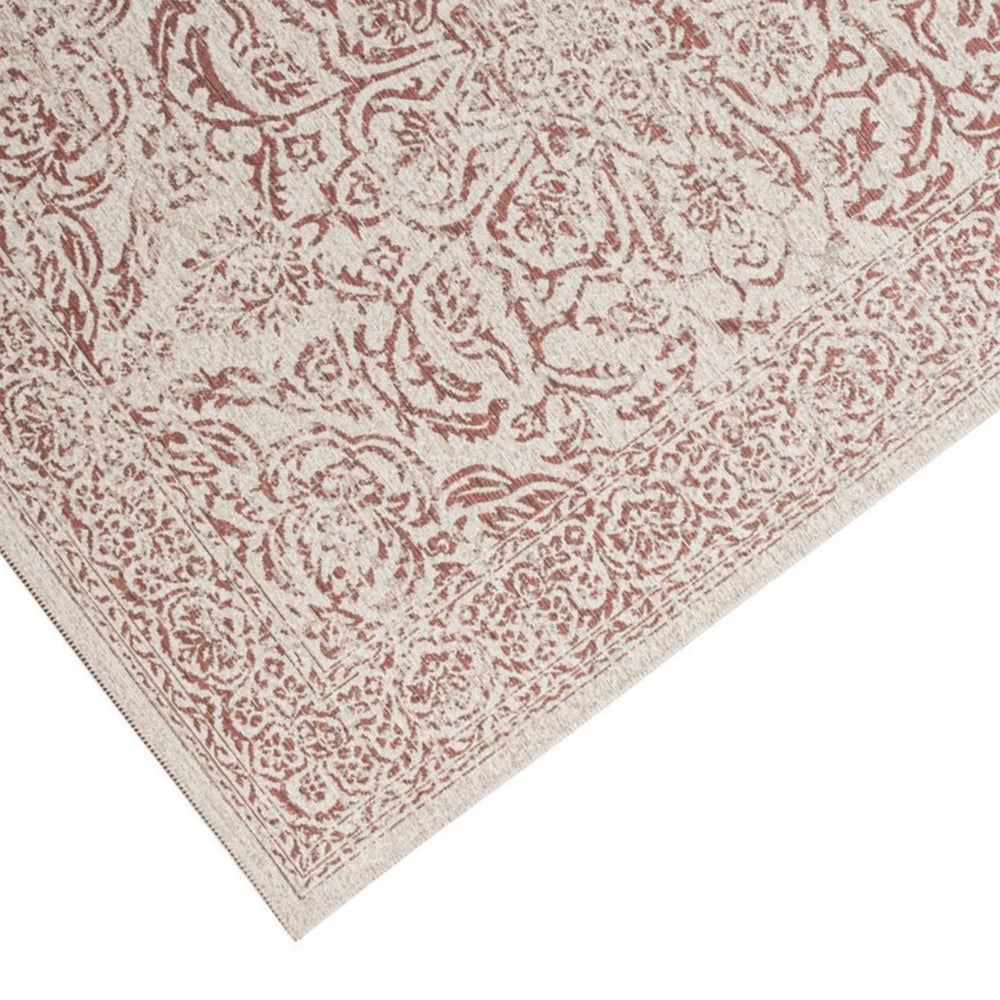 Dettaglio angolo del tappeto con motivo ornamentale rosso su fondo avorio, rifinito con bordo ricco di elementi floreali classici.

