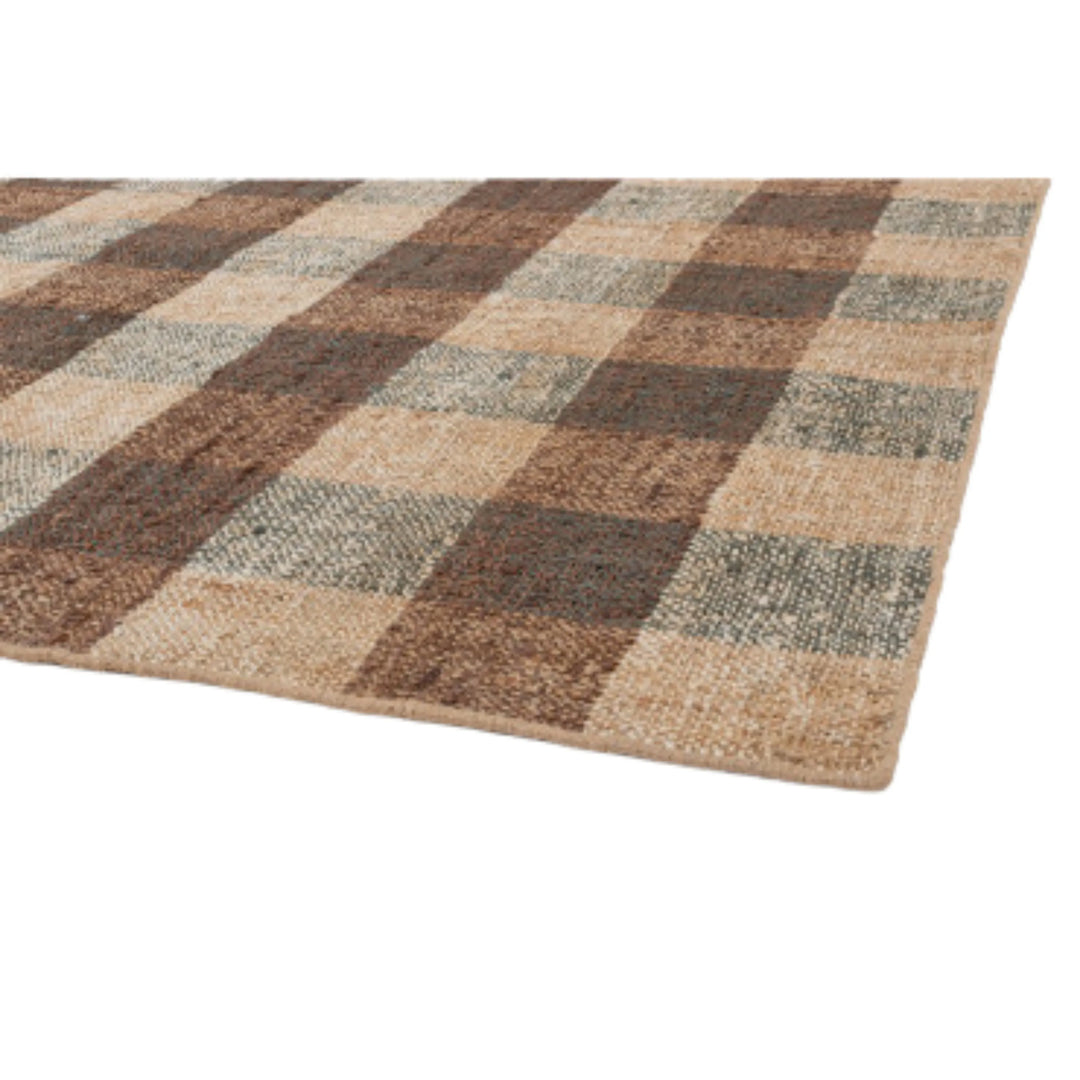 Dettaglio del tappeto in juta con trama intrecciata e pattern a scacchi colorati in beige, marrone e verde salvia, con bordo rifinito a mano.

