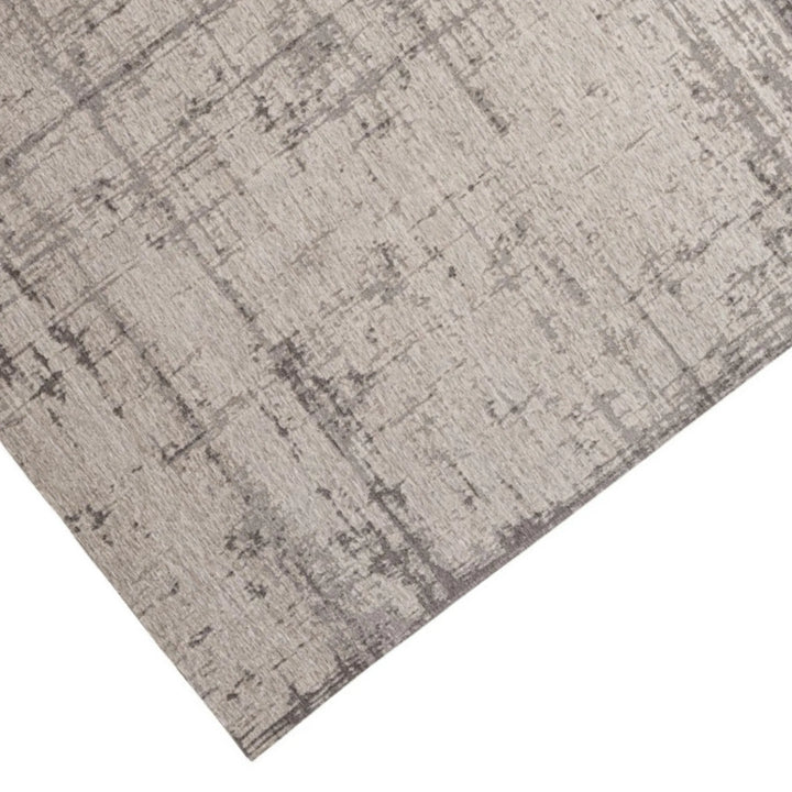 Dettaglio dell’angolo del tappeto moderno con pattern pittorico nei toni grigio-beige, superficie a trama sottile e contemporanea.