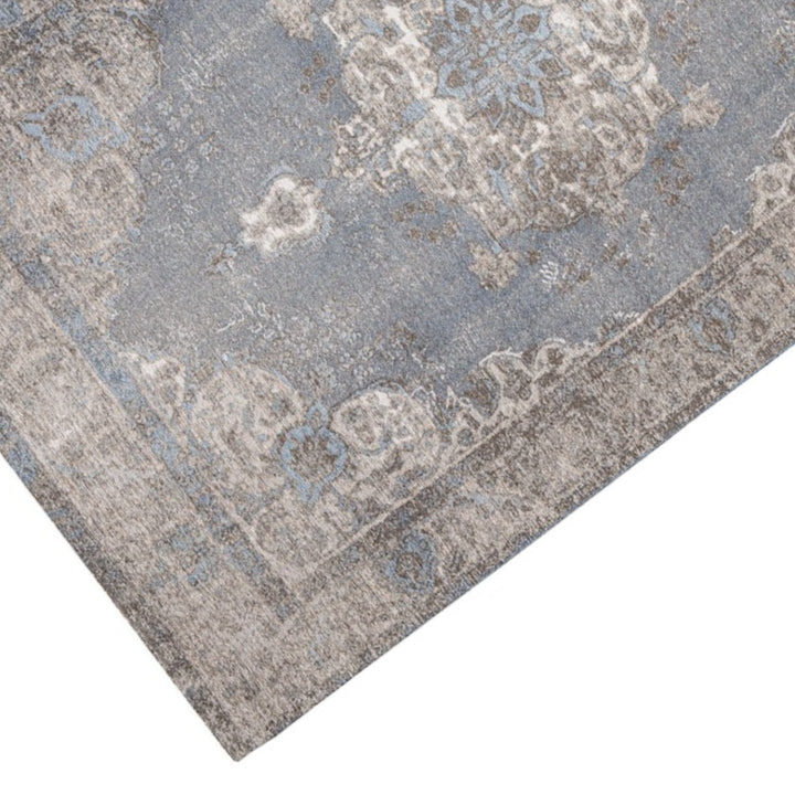 Dettaglio ravvicinato del tappeto effetto antico con disegno floreale nei toni del blu polvere e grigio, texture soffice e look vintage.