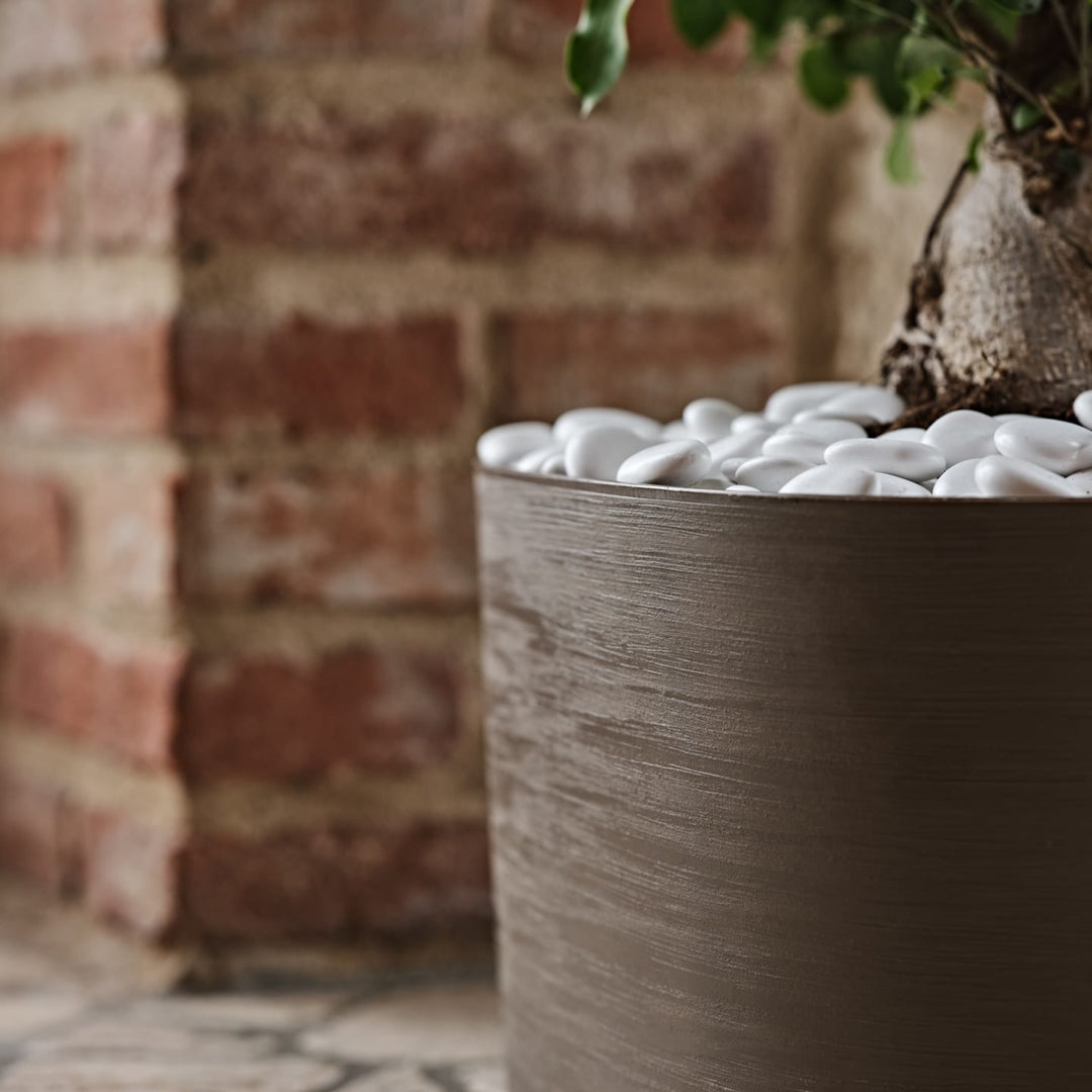 Primo piano di vaso marrone con finitura effetto legno e ciottoli bianchi decorativi.