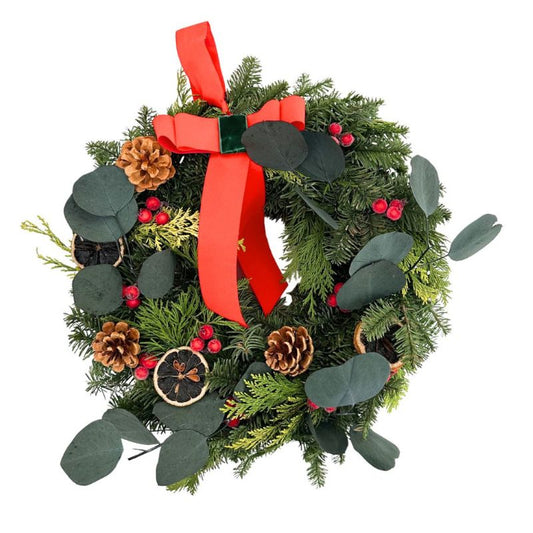 Ghirlanda natalizia realizzata con rami di abete, foglie di eucalipto stabilizzato, pigne, bacche rosse e fette di arancia essiccata, decorata con nastro in velluto rosso.