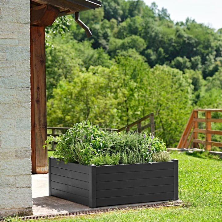 Orto aromatico in vaso rettangolare nero posizionato su una veranda in legno vicino a un'abitazione in pietra, con vista su paesaggio verde.