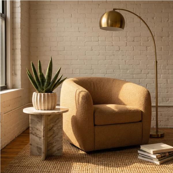 Sansevieria Swasdi in vaso Dioniso su tavolino marmo con poltrona bouclé camel e lampada arco ottone