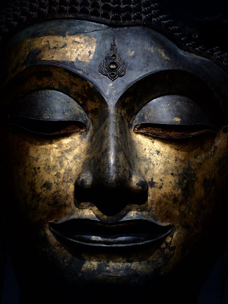 Un volto di Buddha dorato, illuminato in modo suggestivo, con occhi chiusi in meditazione