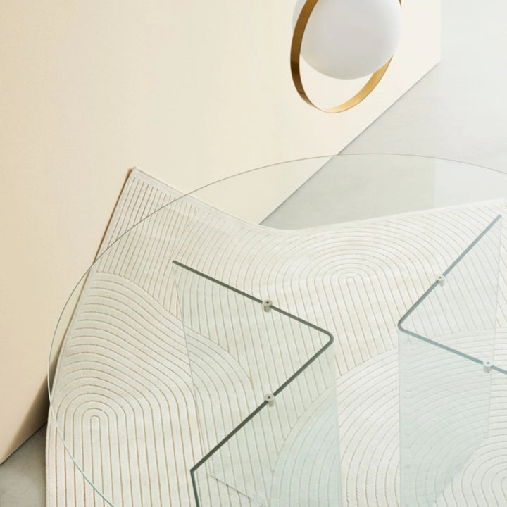 Tappeto avorio moderno con motivi curvi sotto un tavolo rotondo in vetro, in ambiente elegante e minimale.