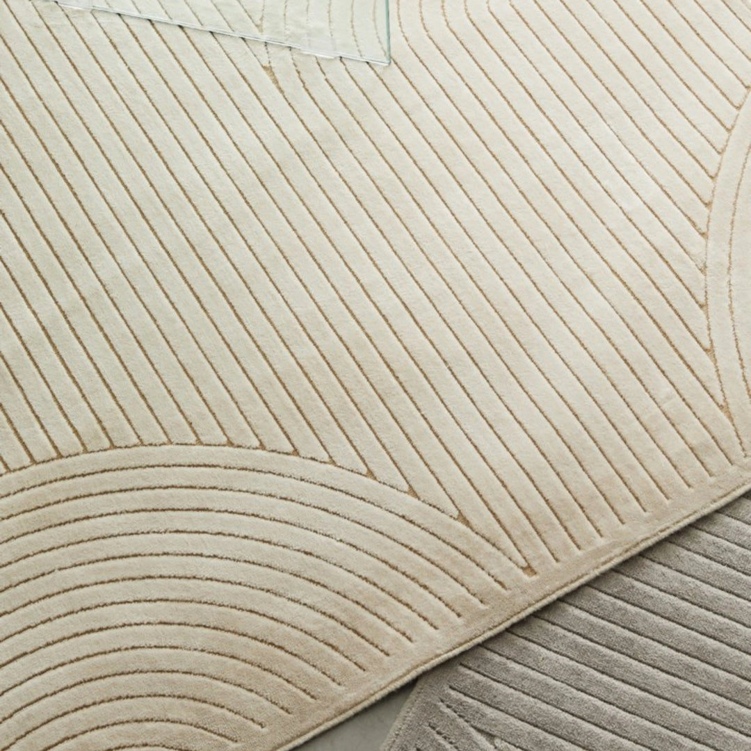 Vista ravvicinata del tappeto avorio a rilievo con pattern arcuato, affiancato da un modello grigio.