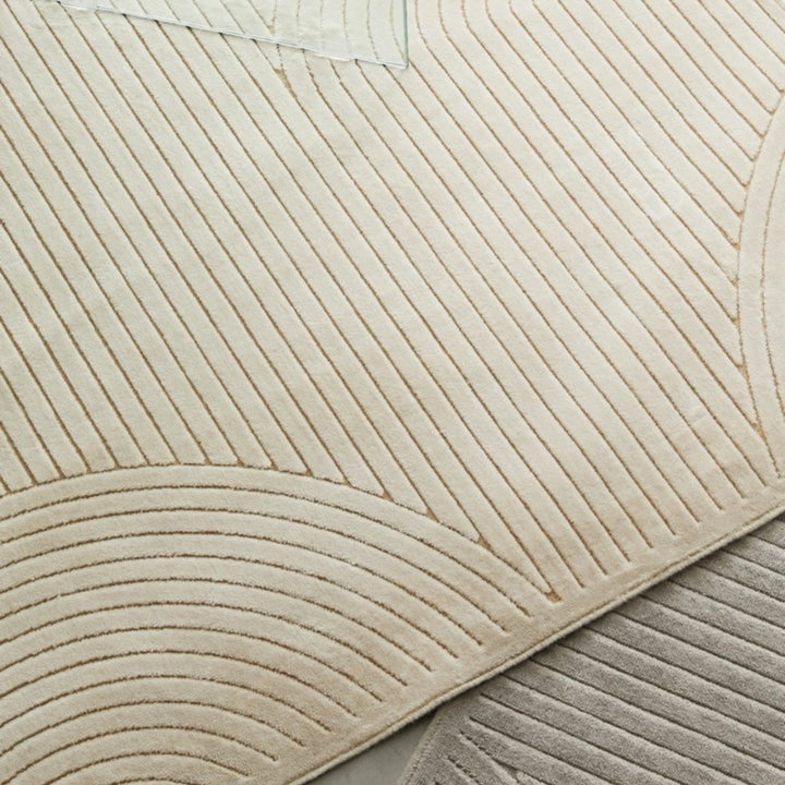 Vista ravvicinata del tappeto avorio a rilievo con pattern arcuato, affiancato da un modello grigio.