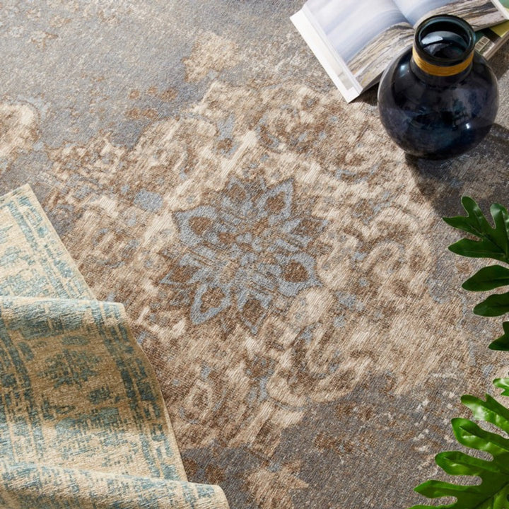 Dettaglio di tappeto classico con motivo floreale centrale in toni azzurro polvere e beige, affiancato da decorazioni e accessori d’arredo in stile naturale.

