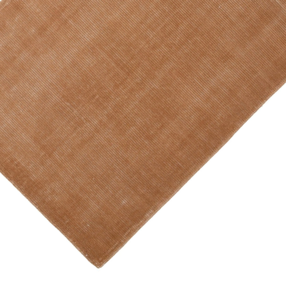 Dettaglio angolo tappeto in fibra naturale color terracotta, con superficie leggermente lucida e trama fine, perfetto per zone living o studio.