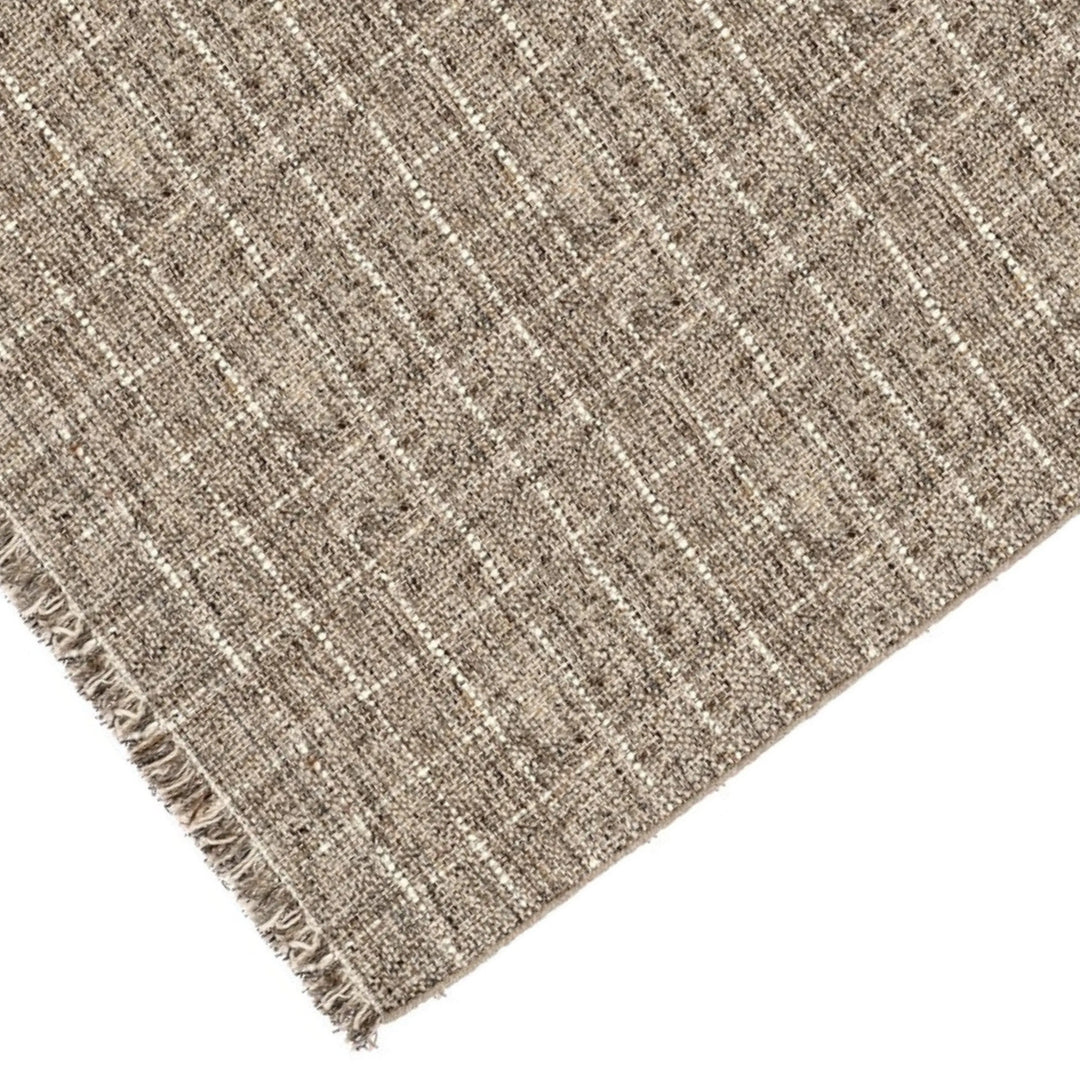 Dettaglio angolare del tappeto in fibra naturale intrecciata con disegno a quadri beige e panna e frange sui bordi.