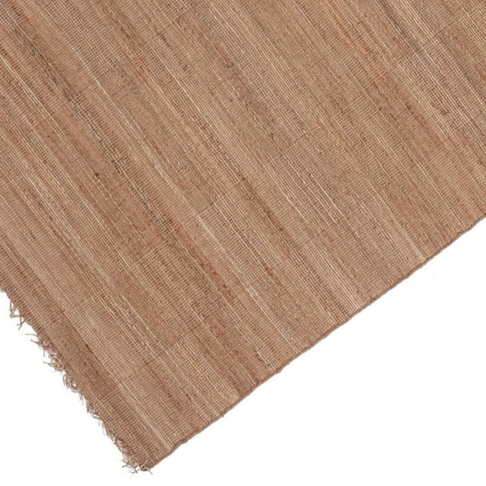 Dettaglio angolare di tappeto in juta naturale con trama sottile e frange decorative.