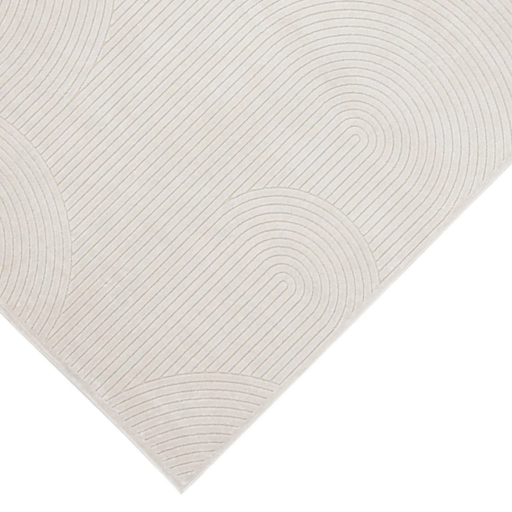 Dettaglio dell’angolo del tappeto moderno avorio con rilievo geometrico a righe curve, su sfondo chiaro.