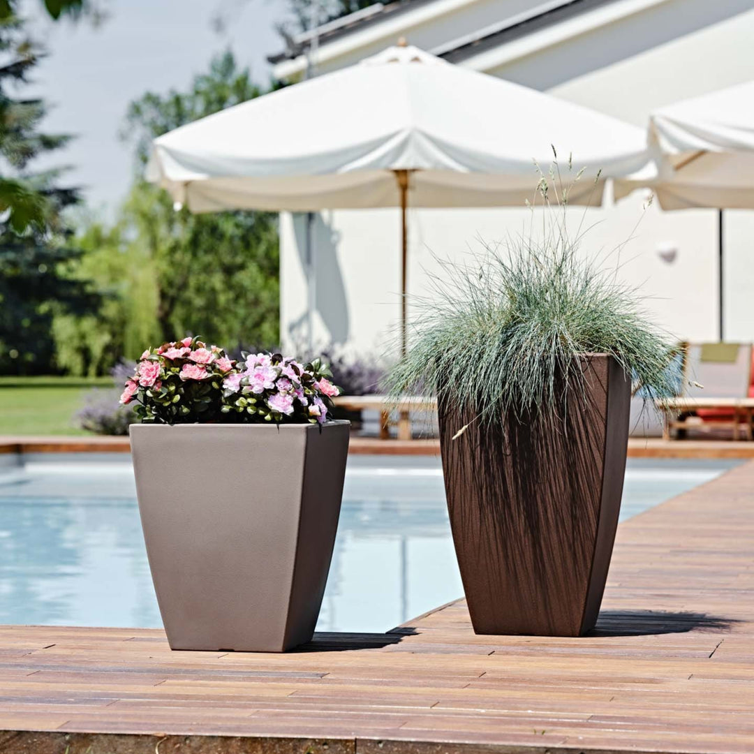 Coppia di vasi alti da esterno posizionati a bordo piscina, contenenti fiori rosa e erba ornamentale, ideali per decorare ambienti outdoor moderni.

