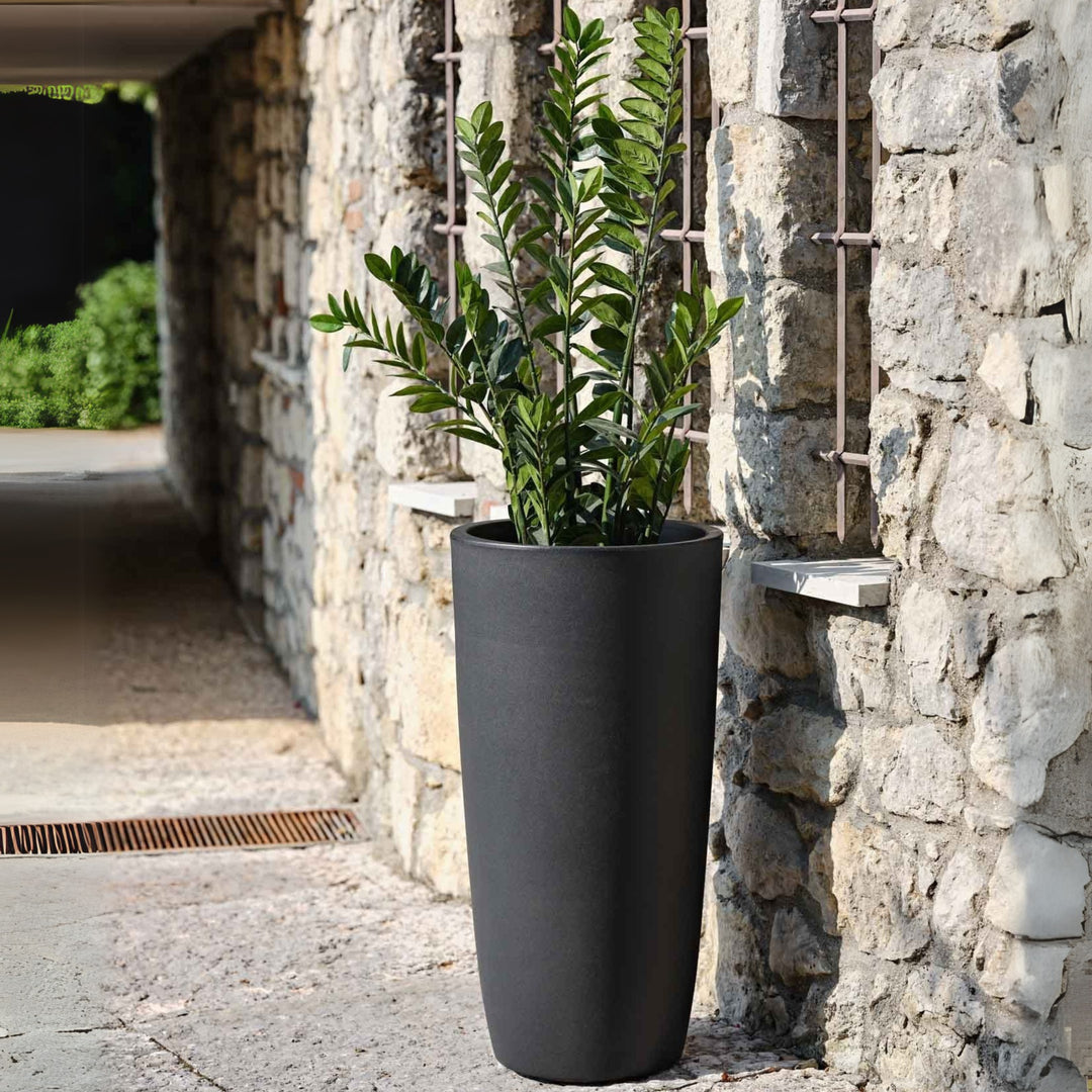 Vaso da esterno alto nero opaco con pianta di Zamioculcas, ambientazione rustica in pietra.