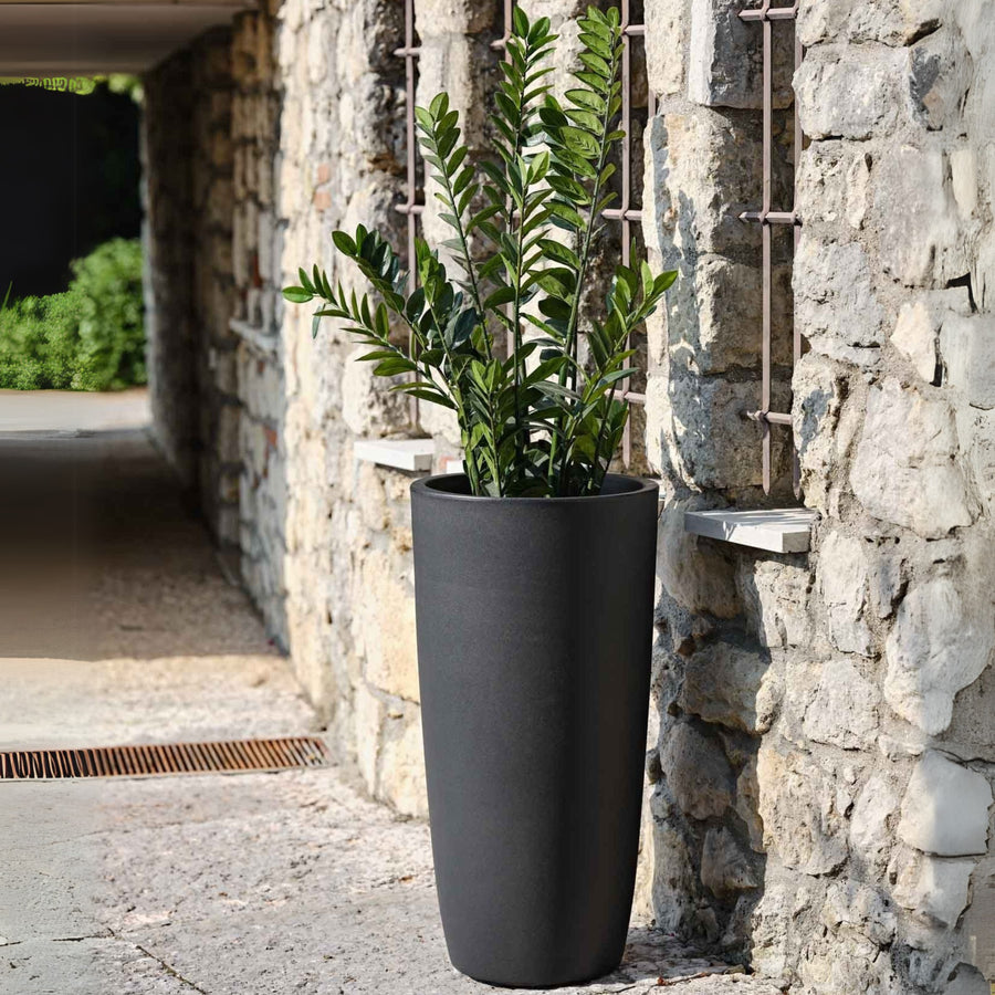 Vaso da esterno alto nero opaco con pianta di Zamioculcas, ambientazione rustica in pietra.