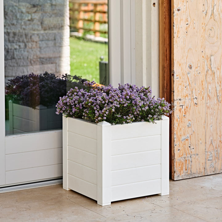 Vaso quadrato bianco con fiori viola posizionato accanto a una porta finestra, su pavimento chiaro — design elegante per arredo outdoor.