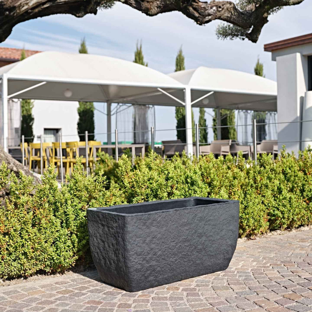 Vaso rettangolare nero effetto pietra posizionato su pavimentazione esterna, ideale per l’arredo outdoor moderno