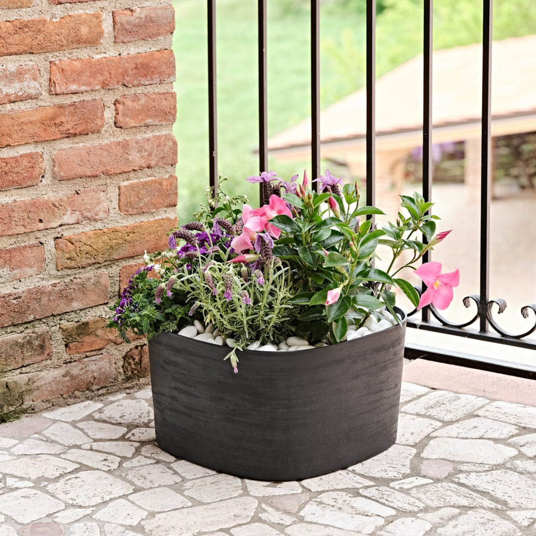 Fiori colorati in vaso nero opaco su balcone in ferro battuto e mattone.

