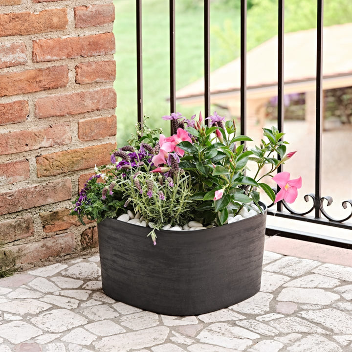 Fiori colorati in vaso nero opaco su balcone in ferro battuto e mattone.

